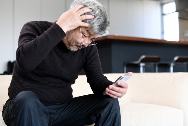 スマホを見て頭を抱える男性