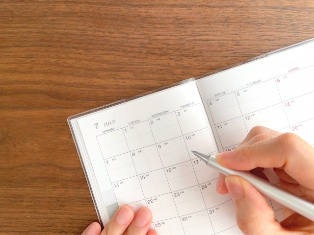 7月のスケジュール帳に記入する女性の手元